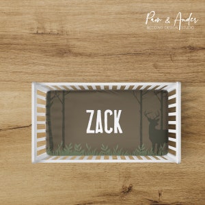 May include: A brown and green cot sheet with a silhouette of a deer and trees. The sheet has the name "ZACK" printed in white on the front.