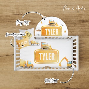 May include: A white crib bedding set with a yellow and orange construction theme. The set includes a fitted sheet, a play mat, and two decorative pillows. The fitted sheet features a large yellow sign with the name "TYLER" on it. The play mat features a yellow construction truck with the name "TYLER" on it. The pillows feature a yellow construction truck and a yellow sign with the name "TYLER" on it.