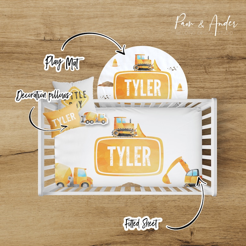May include: A white crib bedding set with a yellow and orange construction theme. The set includes a fitted sheet, a play mat, and two decorative pillows. The fitted sheet features a large yellow sign with the name "TYLER" on it. The play mat features a yellow construction truck with the name "TYLER" on it. The pillows feature a yellow construction truck and a yellow sign with the name "TYLER" on it.