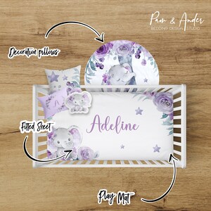 May include: A white cot bedding set with a purple floral and elephant design. The set includes a fitted sheet, a decorative pillow, and a play mat. The fitted sheet has the name "Adeline" embroidered on it.
