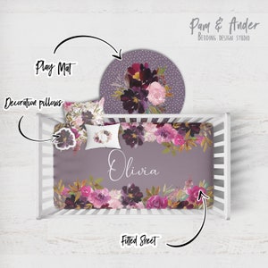 May include: A purple and pink floral cot bedding set with a fitted sheet, a play mat, and decorative pillows. The set features a watercolour floral design with the name "Olivia" printed on the fitted sheet.