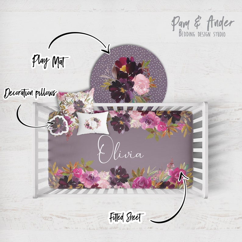 May include: A purple and pink floral cot bedding set with a fitted sheet, a play mat, and decorative pillows. The set features a watercolour floral design with the name "Olivia" printed on the fitted sheet.