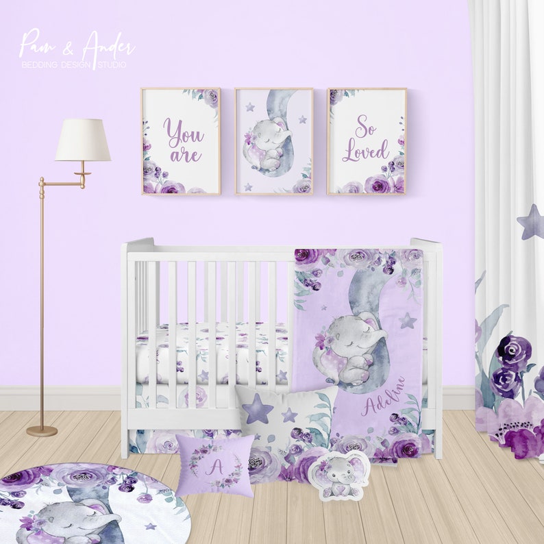 May include: A purple and grey baby nursery bedding set with a floral design and a sleeping elephant. The set includes a cot sheet, a blanket, a pillow, and a round rug. The text "You are So Loved" is on the wall.