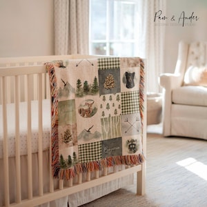 May include: A woven baby blanket with a patchwork design featuring a woodland theme. The blanket has a green, brown, and white color scheme with images of trees, deer, and other woodland creatures. The blanket is fringed on all sides.
