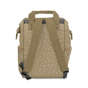 May include: A tan canvas backpack with white polka dots and adjustable straps. The backpack has a top handle and a zippered closure.