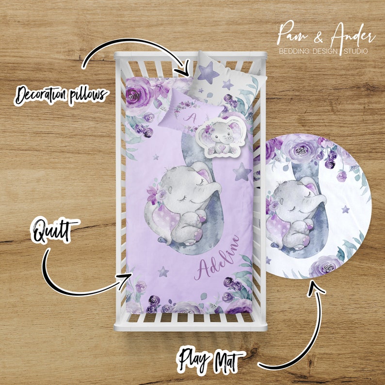 May include: A purple and grey baby bedding set featuring a sleeping elephant design. The set includes a quilt, a play mat, and two decorative pillows. The quilt and play mat feature a watercolour-style elephant with purple flowers and stars. The pillows have a floral design. The set is personalised with the name "Adeline".