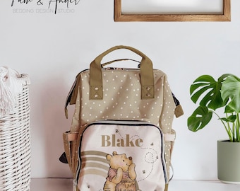 May include: A beige and brown polka dot diaper bag with a Winnie the Pooh character on the front. The bag has a personalized name tag that says "Blake".