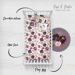 May include: A white cot with a floral patterned fitted sheet and two decorative pillows. A round play mat with a floral design is on the floor next to the cot. The text "Pam & Ander Bedding Design Studio" is in the top right corner of the image.