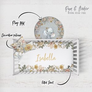 Puede incluir: Una cuna blanca con una s&aacute;bana bajera floral, dos almohadas decorativas y una alfombra de juego redonda con un dise&ntilde;o de elefante. La s&aacute;bana bajera tiene el nombre "Isabella" impreso en ella.