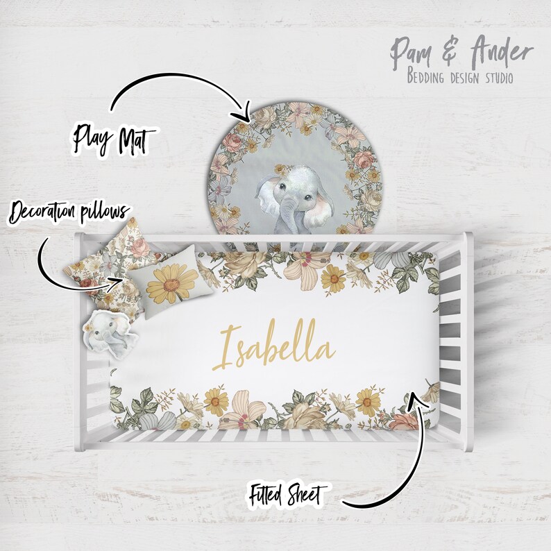 Puede incluir: Una cuna blanca con una s&aacute;bana bajera floral, dos almohadas decorativas y una alfombra de juego redonda con un dise&ntilde;o de elefante. La s&aacute;bana bajera tiene el nombre "Isabella" impreso en ella.