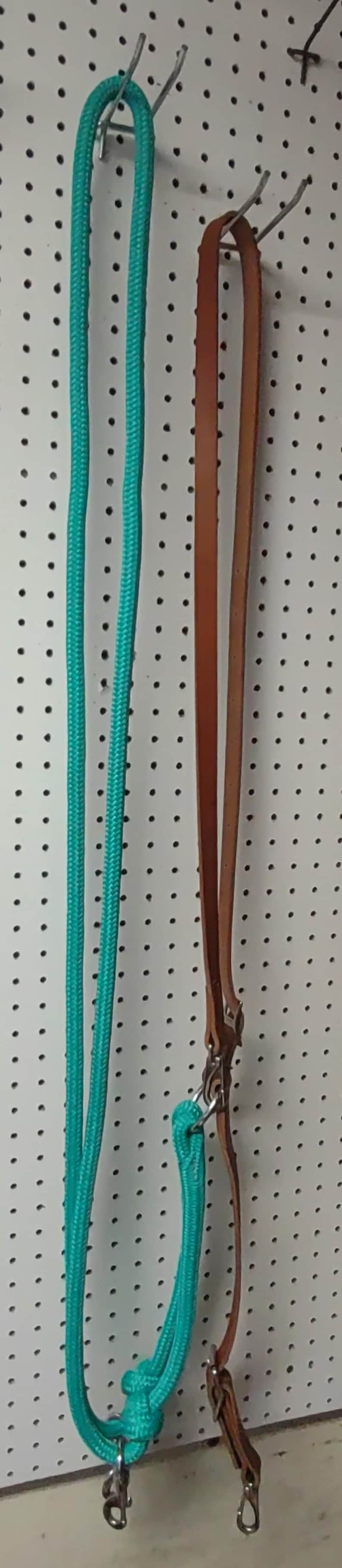 May include: A turquoise rope and a brown leather strap hang against a white pegboard. The rope is looped at the bottom with a metal clasp. The leather strap has a metal clasp and a loop.