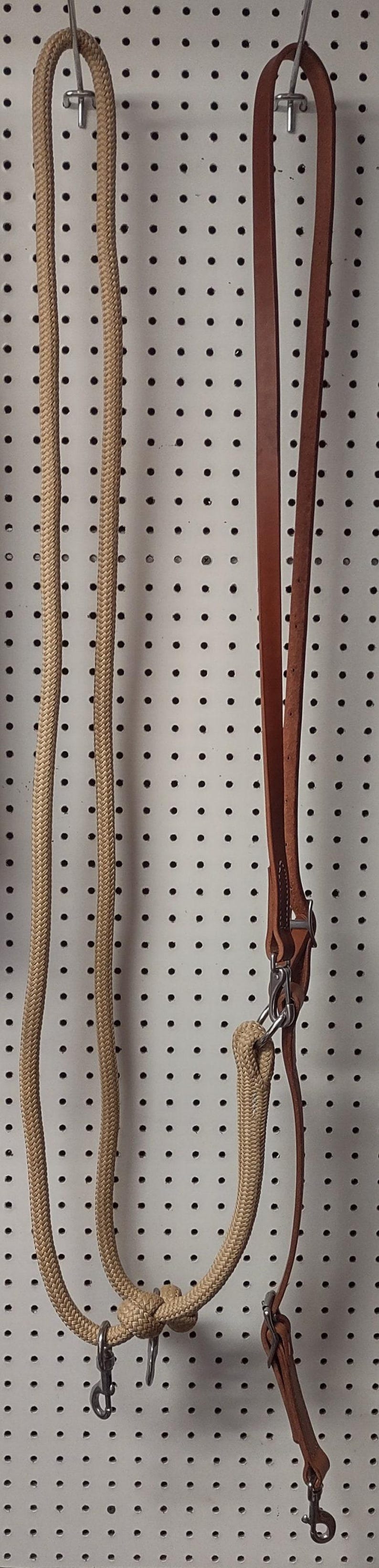 May include: A tan rope and brown leather horse rein set. The rope is braided and attached to a leather strap with metal hardware. The set is designed for equestrian use.