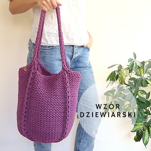 May include: A purple knitted tote bag with a braided strap. The bag is being held by a person wearing blue jeans. The text "WZÓR DZIEWIarski" is visible in the image.