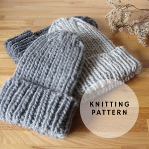May include: Two knitted hats, one gray and one white, with a white circle with the text "Knitting Pattern" on a wooden surface.