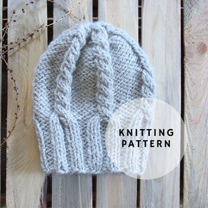 May include: A gray knitted hat with a cable knit pattern. The hat is on a wooden surface with the text "Knitting Pattern" in a white circle.
