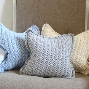 May include: Three knitted throw pillows in a chevron pattern. The pillows are light blue, gray, and cream.