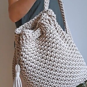 May include: A beige crocheted tote bag with a long strap and a tassel. The bag is made of thick, textured yarn and has a spacious interior.