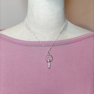 May include: A silver chain necklace with a clear crystal pendant. The pendant is held in a silver ring with a small silver circle above it.