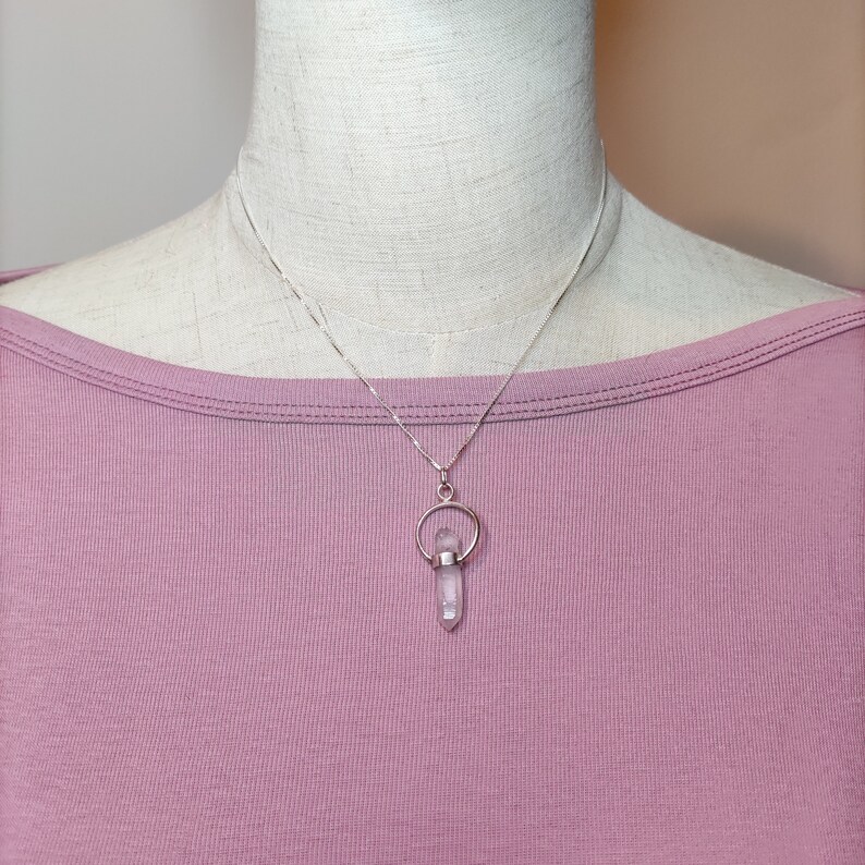 May include: A silver chain necklace with a clear crystal pendant. The pendant is held in a silver ring with a small silver circle above it.