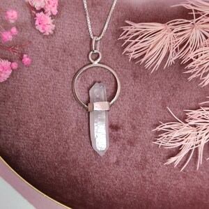 May include: A silver necklace with a clear quartz crystal pendant. The pendant is held in a silver circle and the crystal is pointed at the top.