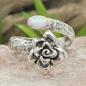 Könnte beinhalten: Ein silberner Ring mit einem weißen Opal-Stein und einem detaillierten Blumendesign. Der Ring ist in Form einer Blume gestaltet und hat einen zarten, femininen Look.
