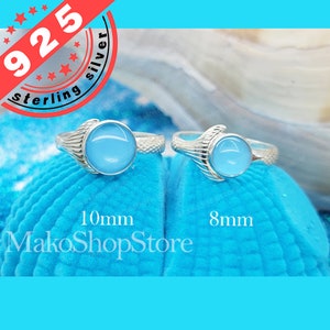 Puede incluir: Dos anillos de plata de ley con engastes de piedras preciosas azules. Los anillos presentan un diseño de cola de sirena. El anillo de la izquierda tiene una piedra de 10 mm y el anillo de la derecha tiene una piedra de 8 mm.