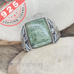 May include: A silver ring with a green stone set in the centre. The ring has an intricate design around the stone, featuring a stylised eagle.