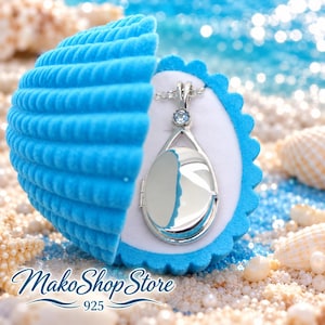 May include: A silver oval locket pendant featuring a small light blue gemstone at the top, presented inside a bright blue velvet seashell-shaped jewelry box. The text MakoShopStore 925 is printed in blue script at the bottom of the image.