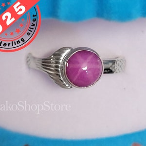 Op de afbeelding: Een ring van sterling zilver met een roze ster-saffier edelsteen. De ring heeft een delicaat, bladvormig ontwerp op de band.