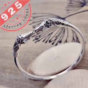 May include: Sterling silver bangle bracelet featuring two horse head charms facing each other. The bracelet is open and has a polished finish.