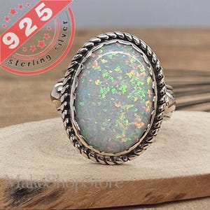 May include: A silver ring with a white opal gemstone set in a rope-like design. The ring is marked "925 sterling silver".
