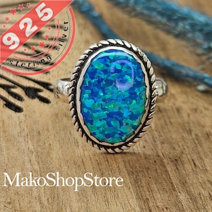 May include: A silver ring with a blue opal gemstone set in a rope-like border. The ring is on a wooden surface.
