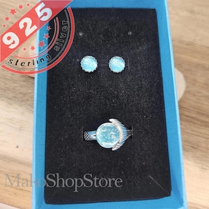 May include: A set of sterling silver jewelry featuring a ring and earrings with a blue, sparkly stone. The ring has a delicate design with a small wing on each side of the stone. The jewelry is displayed in a blue box with the text "MakoShopStore".