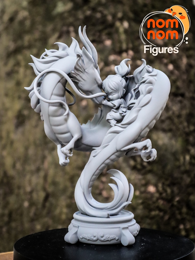 K&ouml;nnte beinhalten: Eine graue, detaillierte Figur eines Drachen und einer kleinen menschlichen Figur. Der Drache ist um den Menschen herumgewickelt, und die beiden Figuren ber&uuml;hren sich mit der Nase. Die Figur steht auf einem runden Sockel mit einem dekorativen Design.