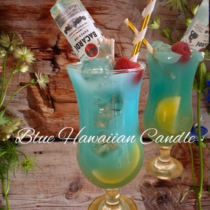 May include: Two blue Hawaiian cocktails with a yellow lemon wedge and a red cherry garnish. The cocktails are in tall glasses and have a blue curacao base. The text 