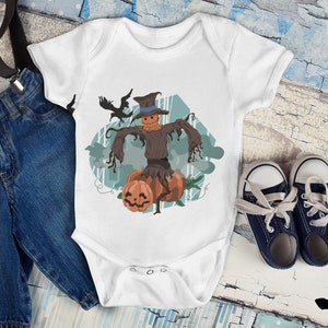 May include: White baby onesie with a graphic of a scarecrow with a pumpkin in each hand. The scarecrow is wearing a brown hat and has a black crow flying above it. The onesie is on a wooden background with blue jeans and suspenders.