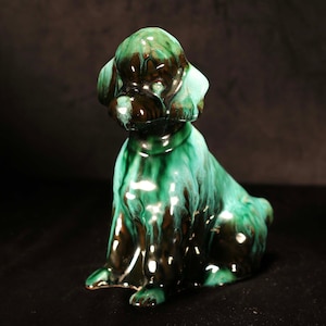 May include: A green and brown glazed ceramic poodle figurine. The poodle is sitting with its head tilted to the side.