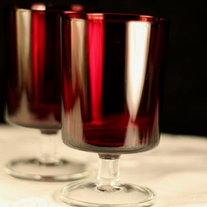 May include: Two clear glass goblets with a deep red hue. The goblets have a round base and a wide bowl.