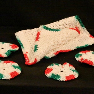 Può includere: Set di cinque sottobicchieri all'uncinetto in rosso, bianco e verde. I sottobicchieri hanno la forma di un fiore con un foro al centro. Un pezzo più grande all'uncinetto è piegato a metà ed è anche di colore rosso, bianco e verde.