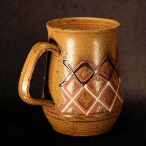 Puede incluir: Una taza de cer&aacute;mica marr&oacute;n con asa y un dise&ntilde;o geom&eacute;trico de diamantes blancos, rojos y negros.