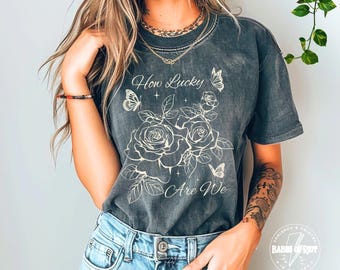 Camiseta "Qué suerte tenemos": Camiseta cristiana con estampado floral y mariposas en colores cómodos