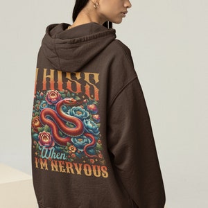 Könnte beinhalten: Ein brauner Hoodie mit einem Grafikdruck eines roten Schlangens mit Blumen und dem Text "I hiss when I'm nervous".