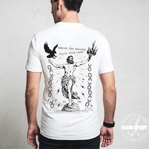 Könnte beinhalten: Weißes T-Shirt mit einem schwarzen Grafikdruck eines Mannes, der eine Fackel hält und Ketten zerbricht. Der Text "BREAK THE CHAINS CLAIM YOUR LIGHT" ist auf das Shirt gedruckt.
