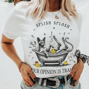 May include: White t-shirt with a black and white illustration of a hairless cat in a bathtub with rubber duckies. The text "Splish Splash Your Opinion Is Trash" is printed on the shirt.