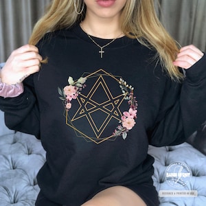 May include: Black sweatshirt with a gold geometric star design surrounded by pink and white flowers.