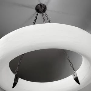 May include: A white circular pendant light fixture with a textured surface hangs from a chain. The light fixture has a large opening in the center.