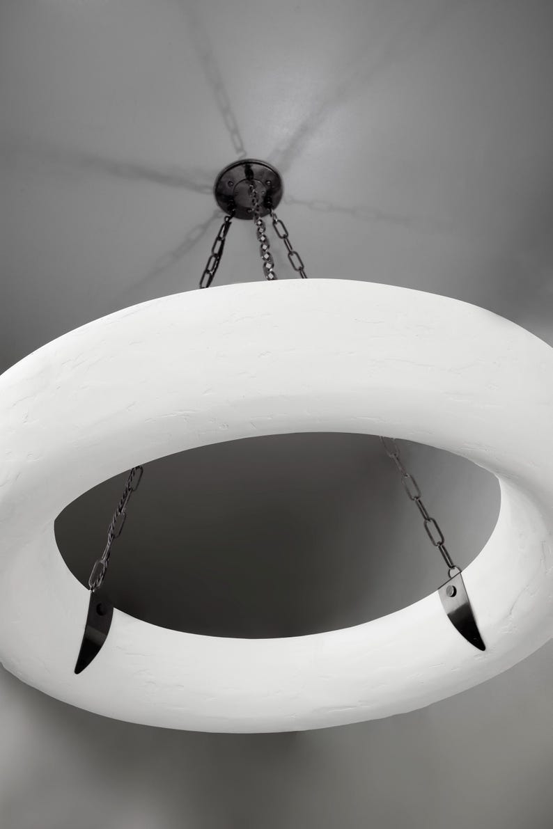 May include: A white circular pendant light fixture with a textured surface hangs from a chain. The light fixture has a large opening in the center.