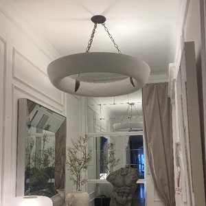 May include: A white circular pendant light fixture with a ring design hangs from a chain in a hallway with white walls and a mirror.