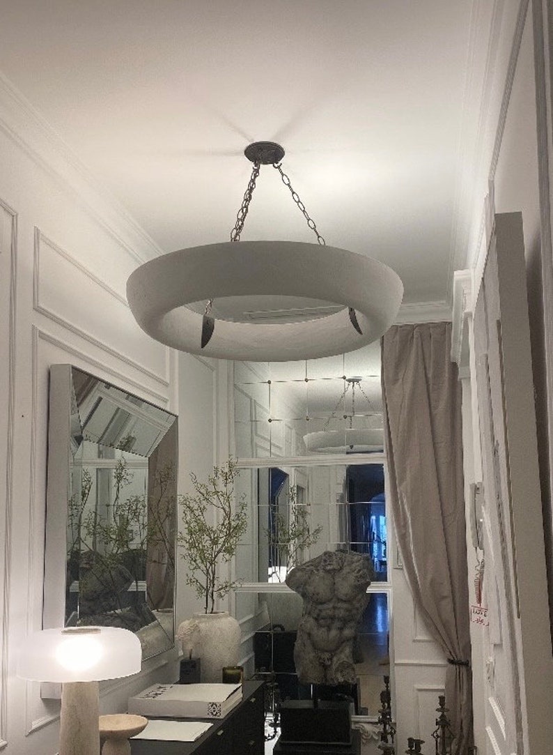 May include: A white circular pendant light fixture with a ring design hangs from a chain in a hallway with white walls and a mirror.