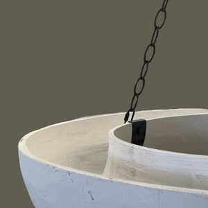 May include: White hanging planter with a black chain. The planter is made of a textured material and has a rounded shape.